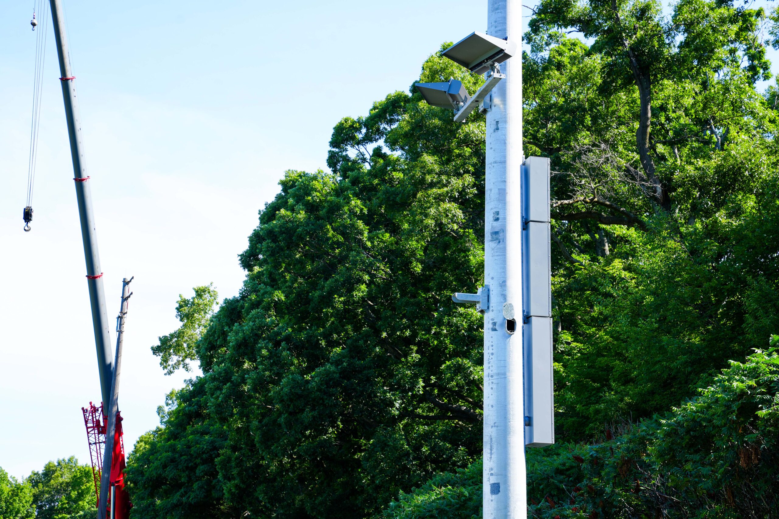 Close-up of a Buist-installed stadium light pole showing LED fixtures and mounted electrical equipment, with a crane in the background.