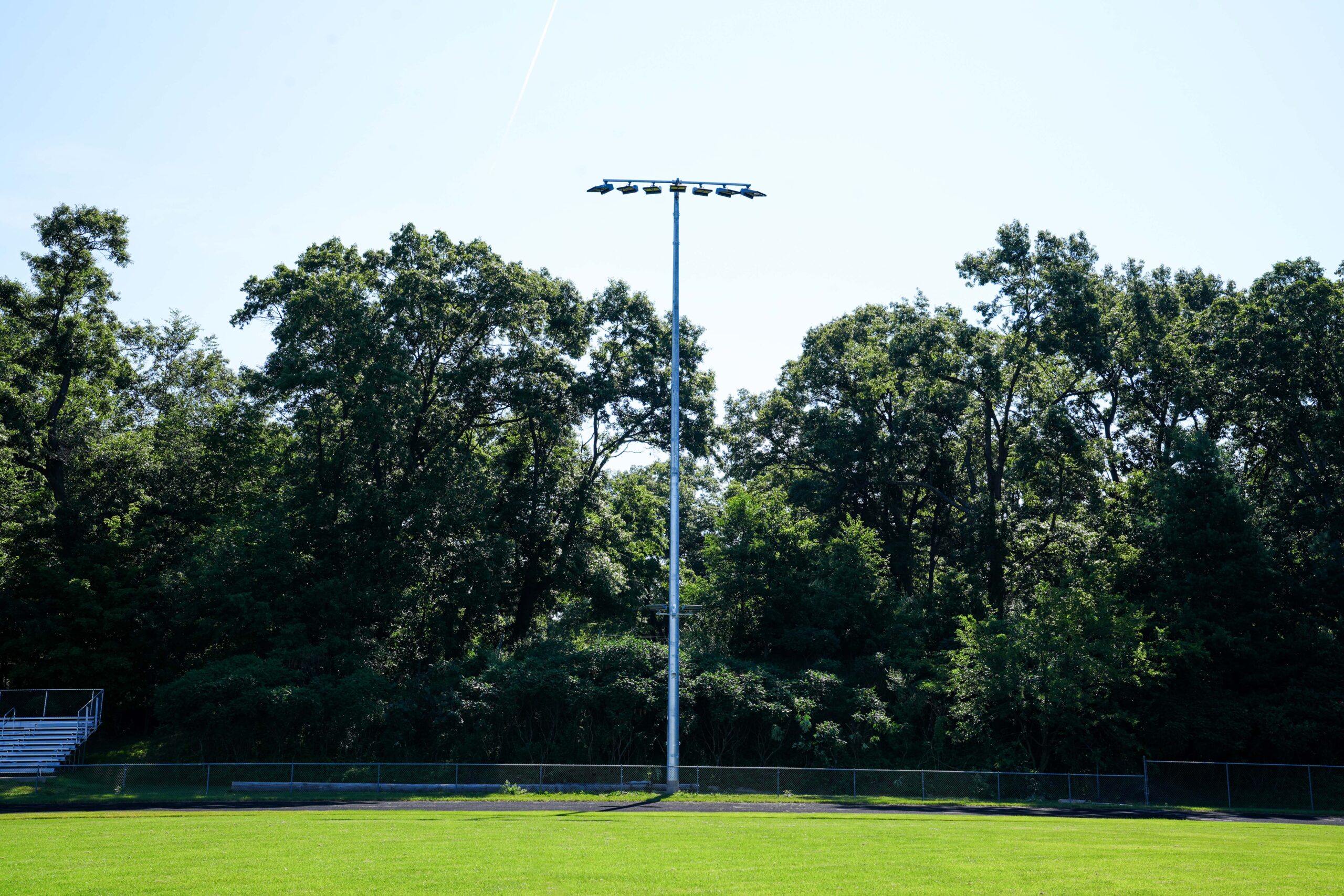 Buist-installed stadium LED light pole standing tall against a backdrop of green trees at an outdoor athletic field.