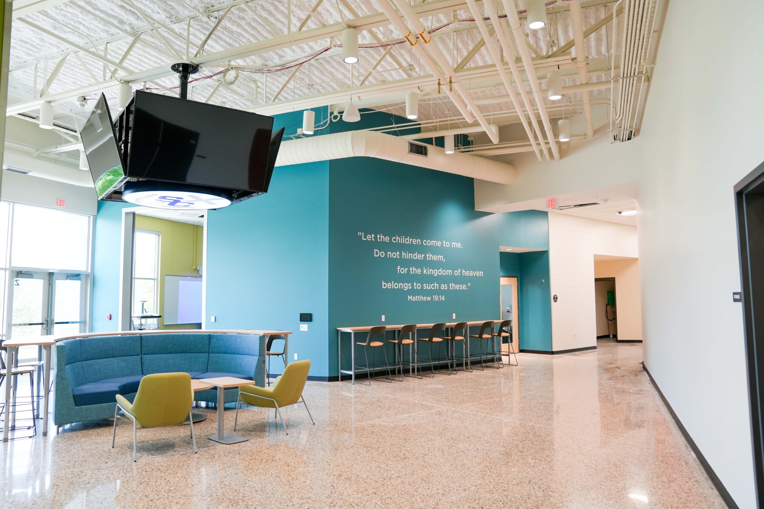 Open lounge area at South Christian High School with scripture wall from Matthew 19:14, designed with Buist’s electrical and lighting systems.