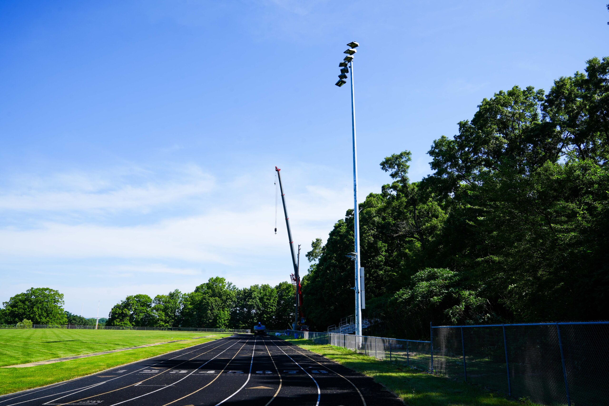 View of a track and field with a Buist-installed stadium light pole and crane positioned along the sideline during installation