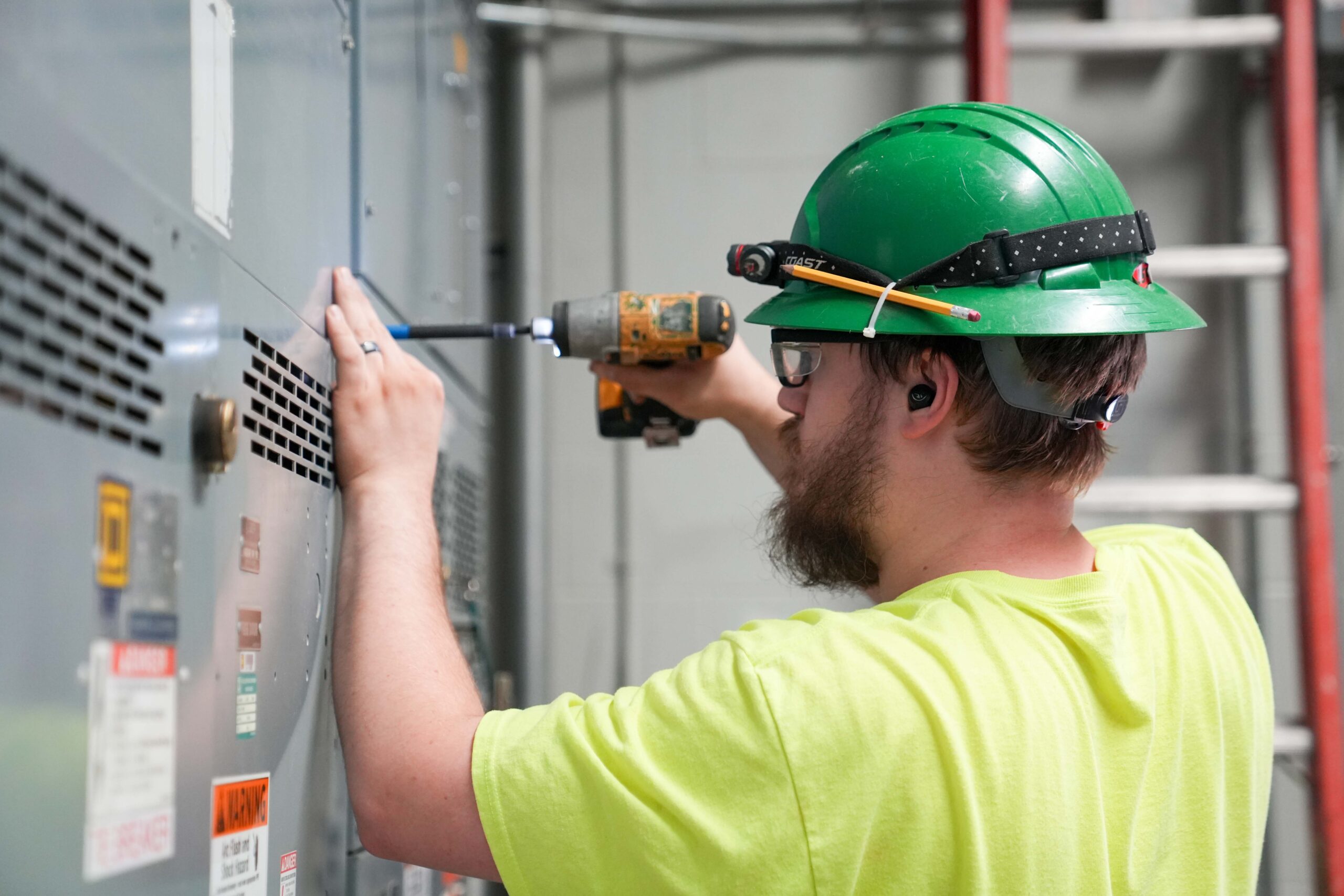Buist electrician using a power drill on switchgear panel during maintenance.
