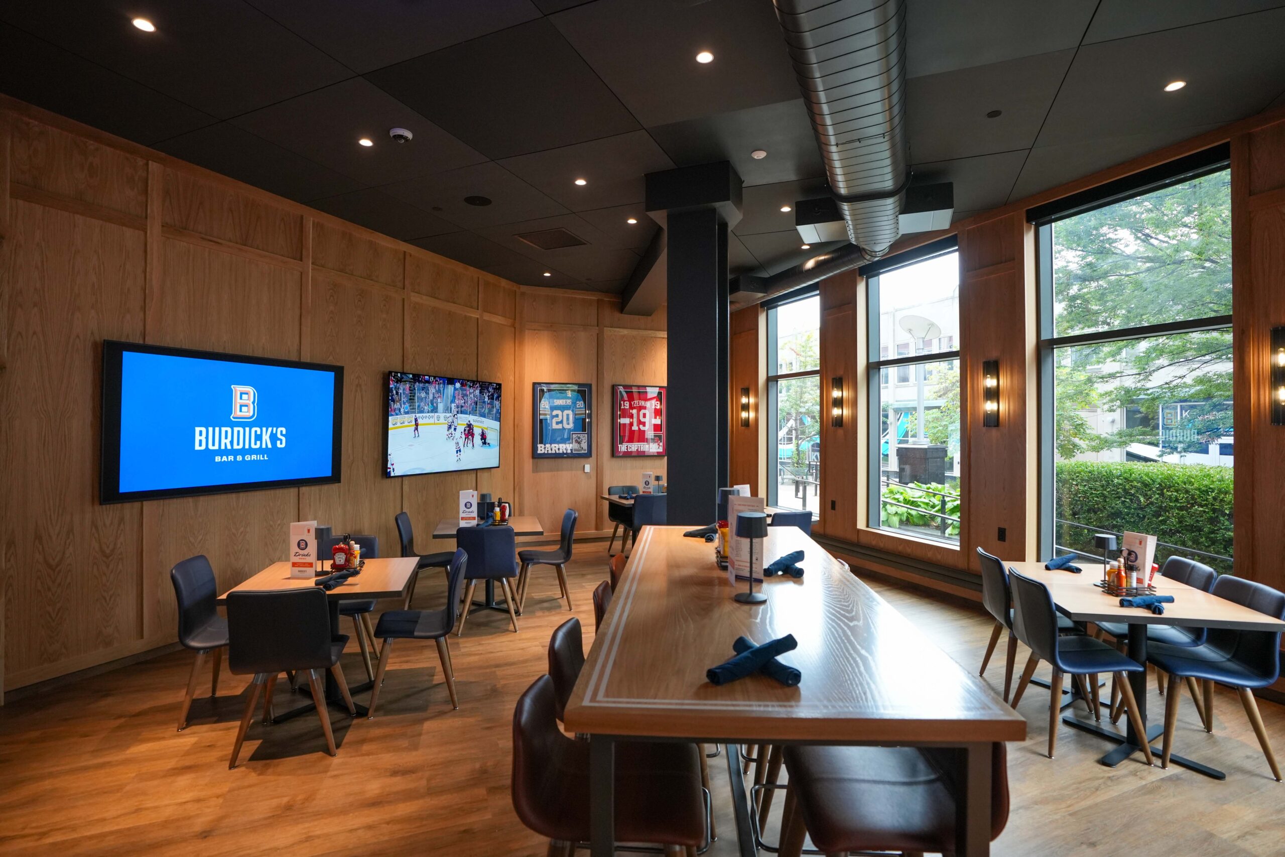Corner dining area at Burdick’s with mounted video displays and natural window light.
