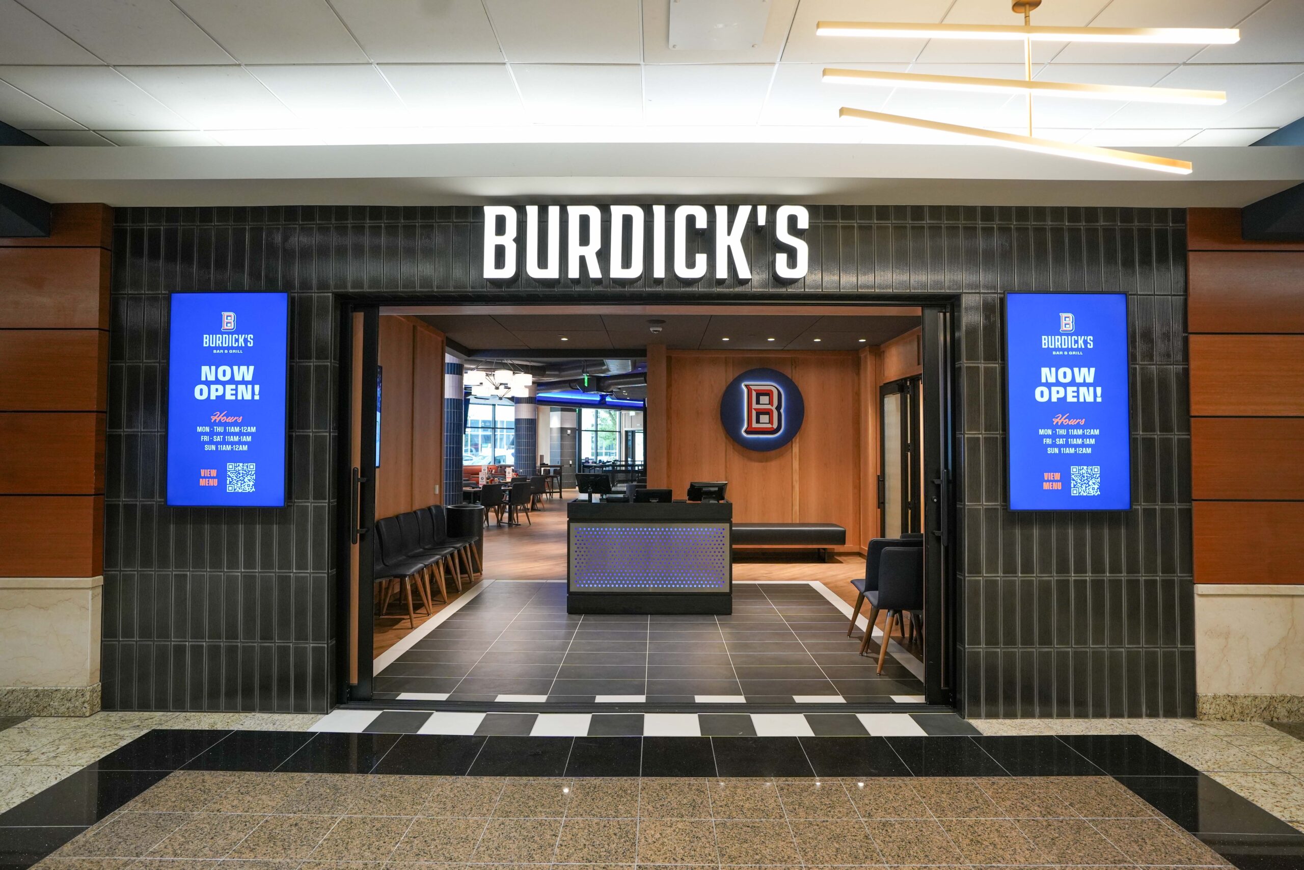 Exterior entrance to Burdick’s Bar & Grill at the Radisson Plaza Hotel with digital “Now Open” signage.