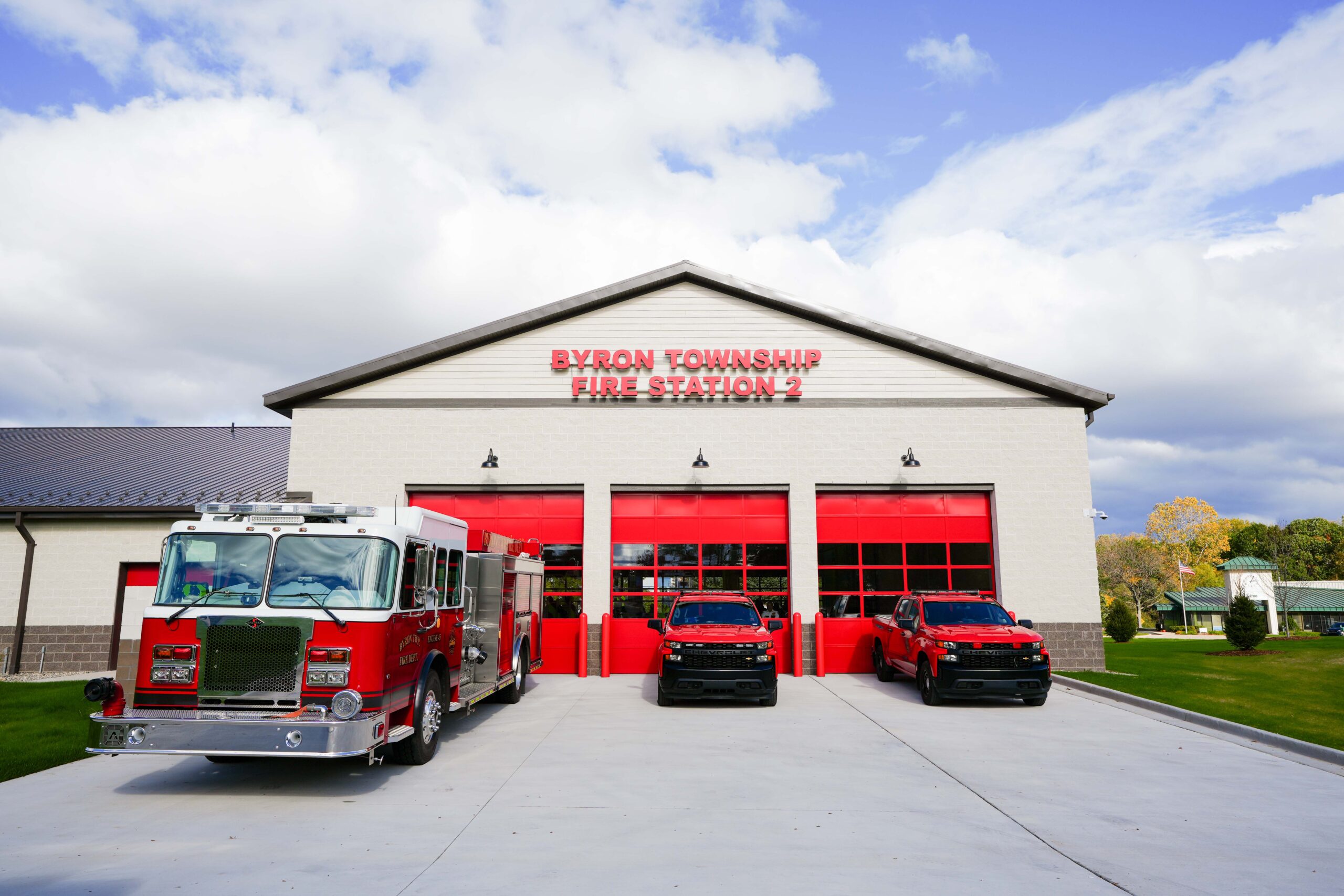 Front view of Byron Township Fire Station No. 2 with fire engines parked outside the building’s bright red bay doors.
