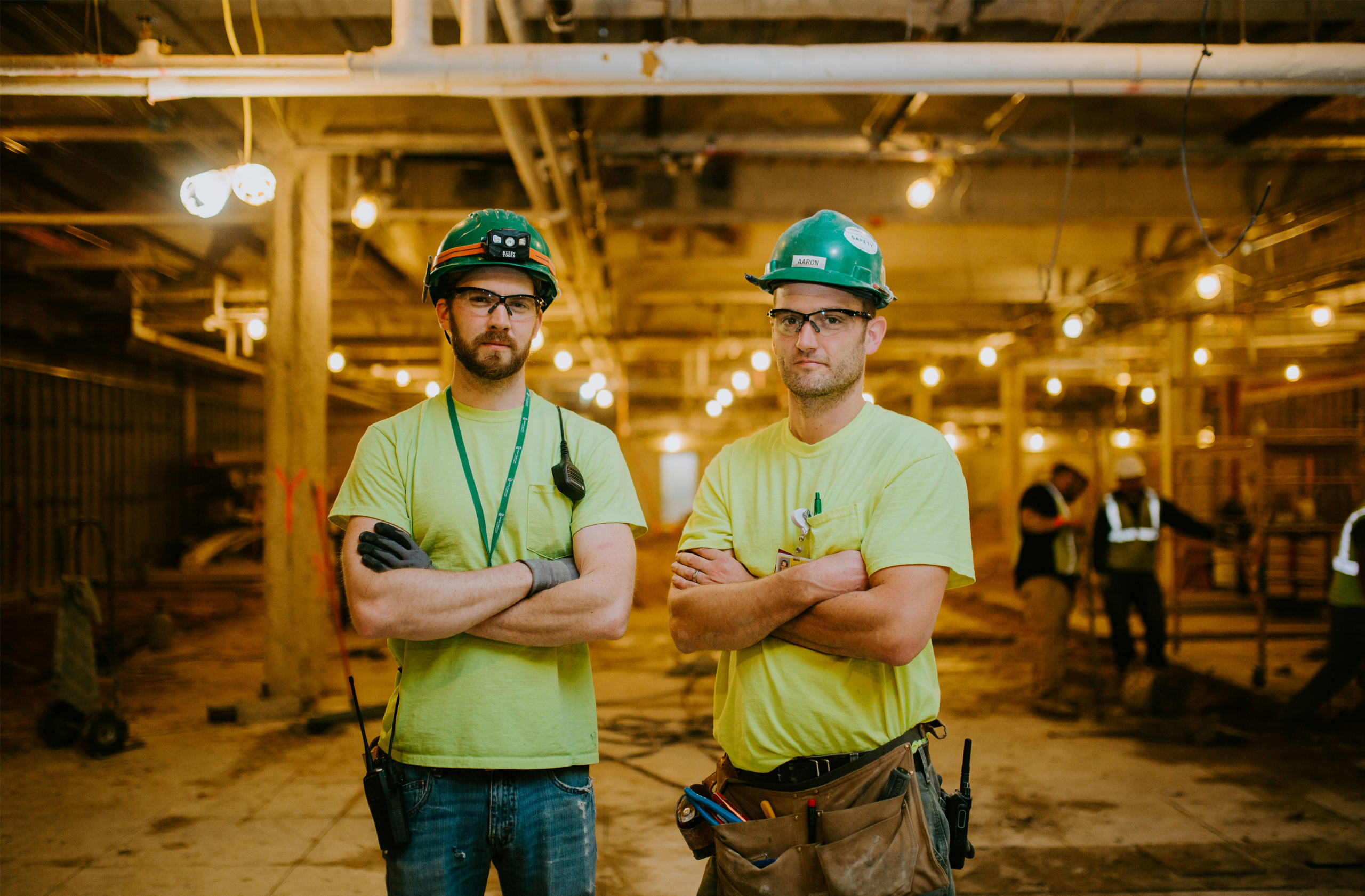 Two Buist electricians standing inside a commercial construction project in West Michigan wearing safety gear and tool belts.