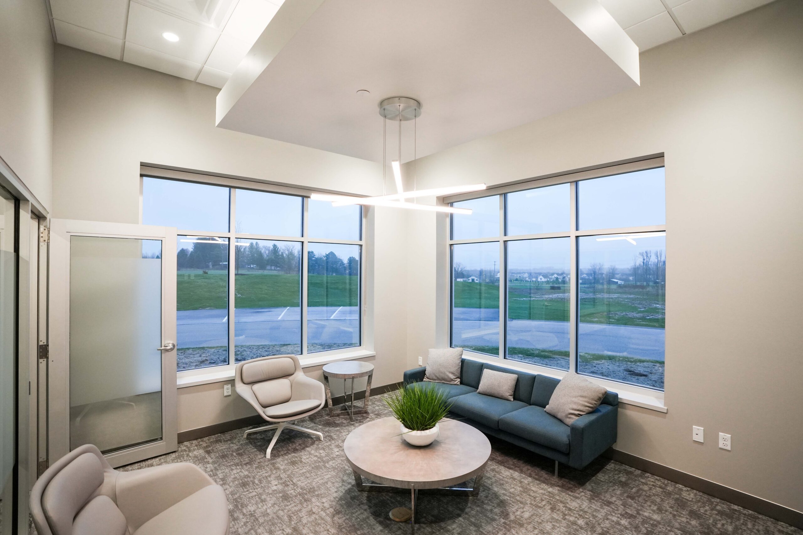 Office collaboration hallway with glass conference rooms, lounge seating, and integrated lighting systems.