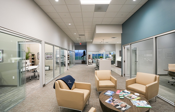 Modern office collaboration hallway with glass conference rooms, lounge seating, and integrated commercial lighting systems.