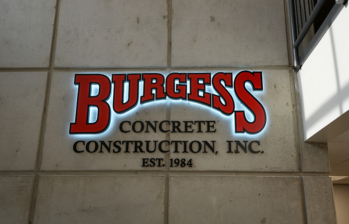 Backlit Burgess Concrete Construction logo mounted on an interior concrete wall in the company's renovated headquarters.