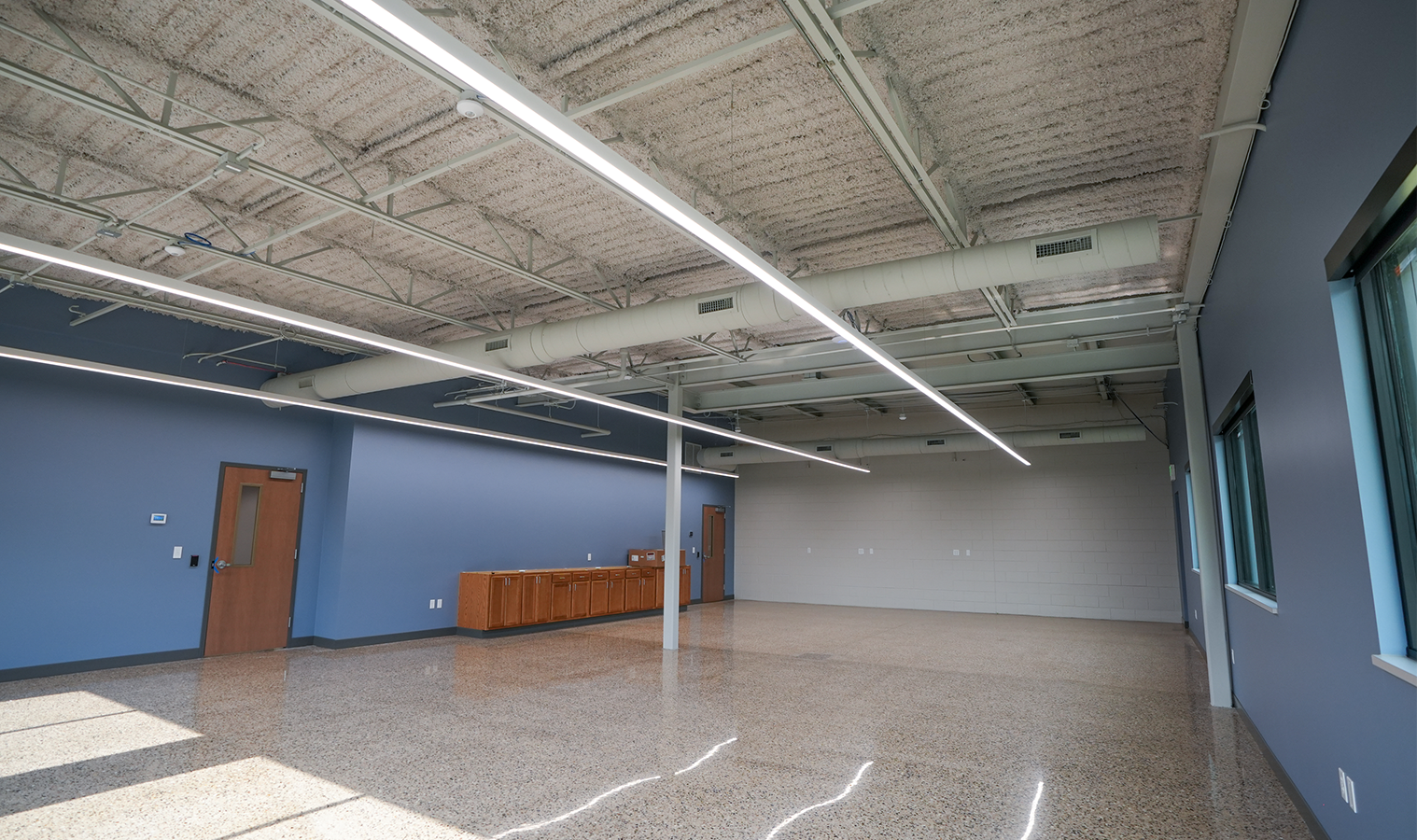 Open office area featuring polished concrete floors, linear LED lighting, and exposed ceiling elements at Burgess Concrete Construction.