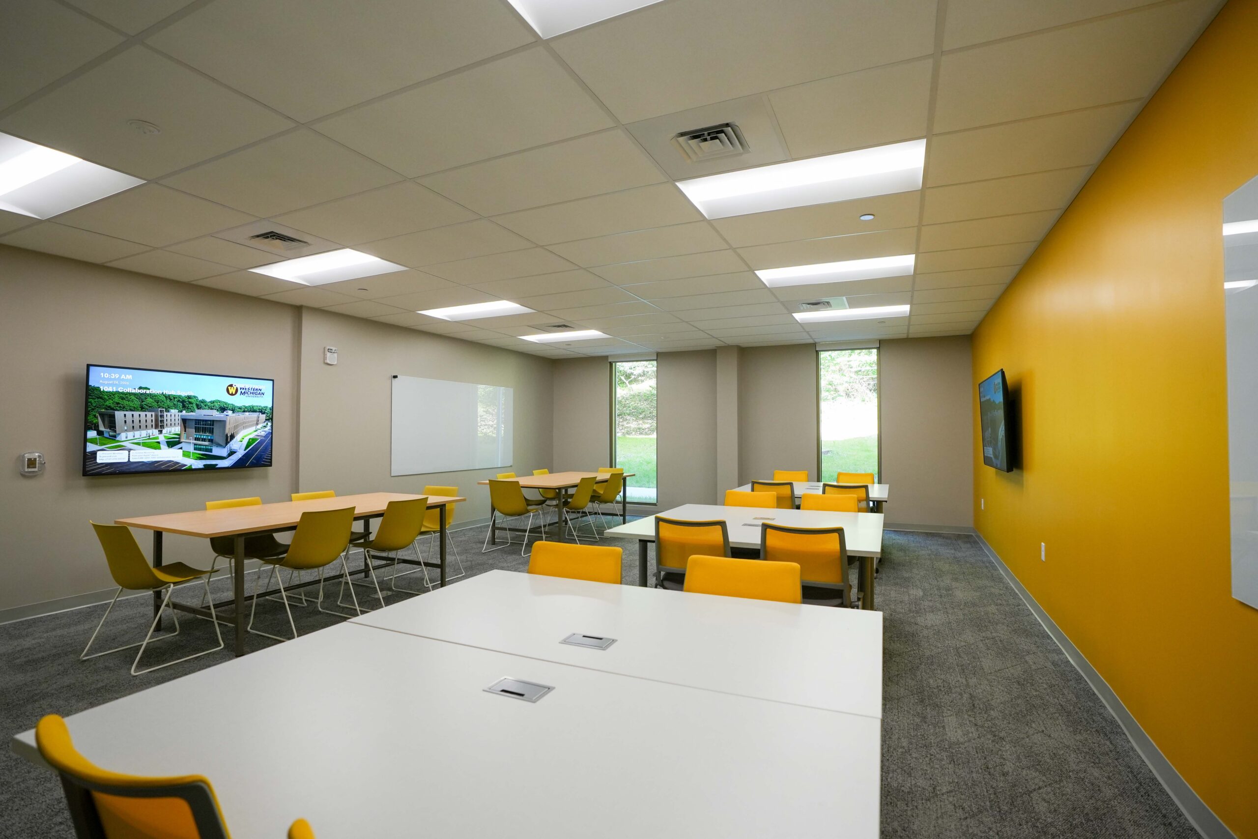 Western Michigan University Valley Oaks collaboration hub with yellow chairs, group study tables, and wall-mounted displays.