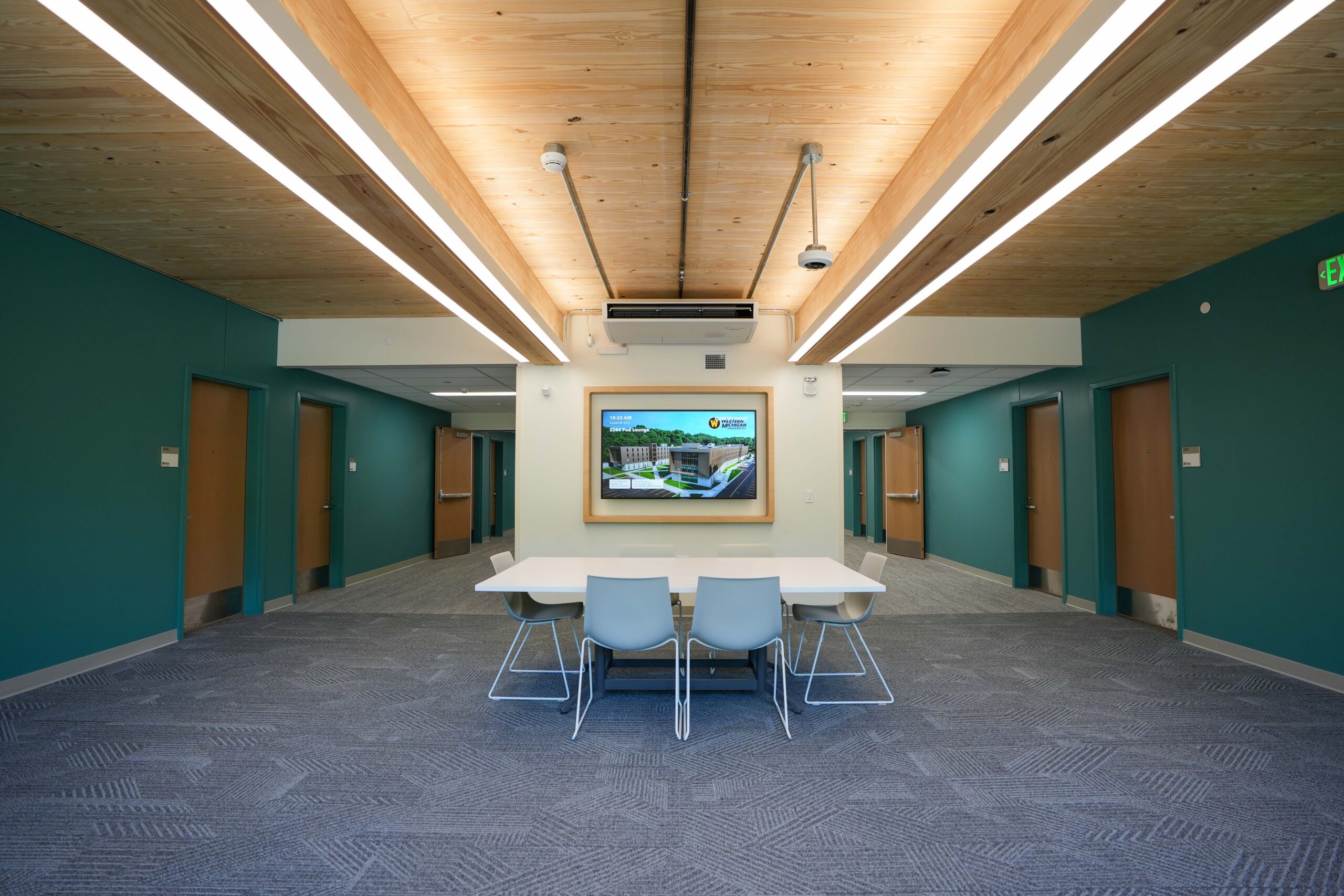 Western Michigan University Valley Oaks pod lounge featuring a wall-mounted digital display, study table, and teal accent walls.