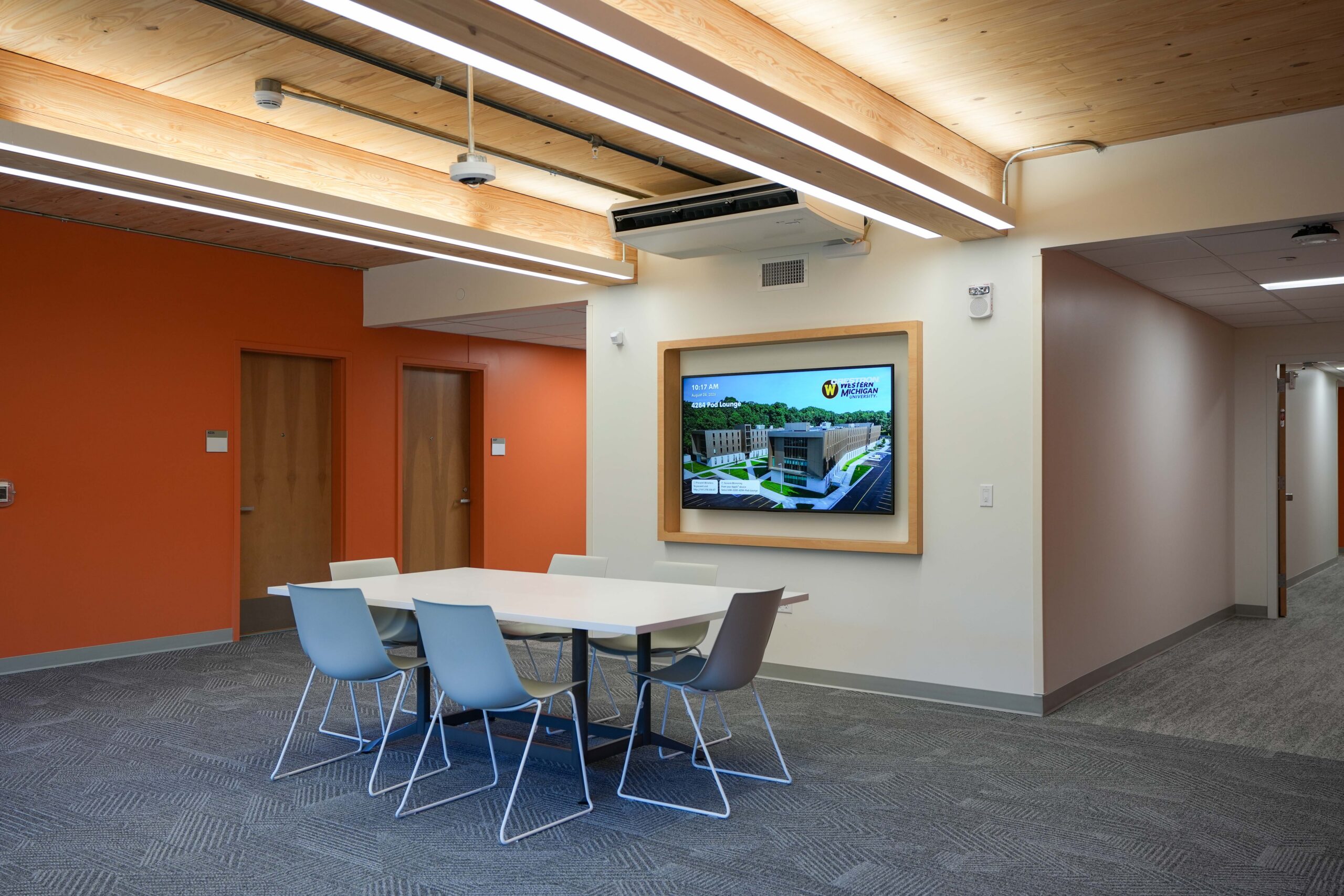WMU Valley Oaks student collaboration space with a wall-mounted display, group study table, and exposed timber ceiling.