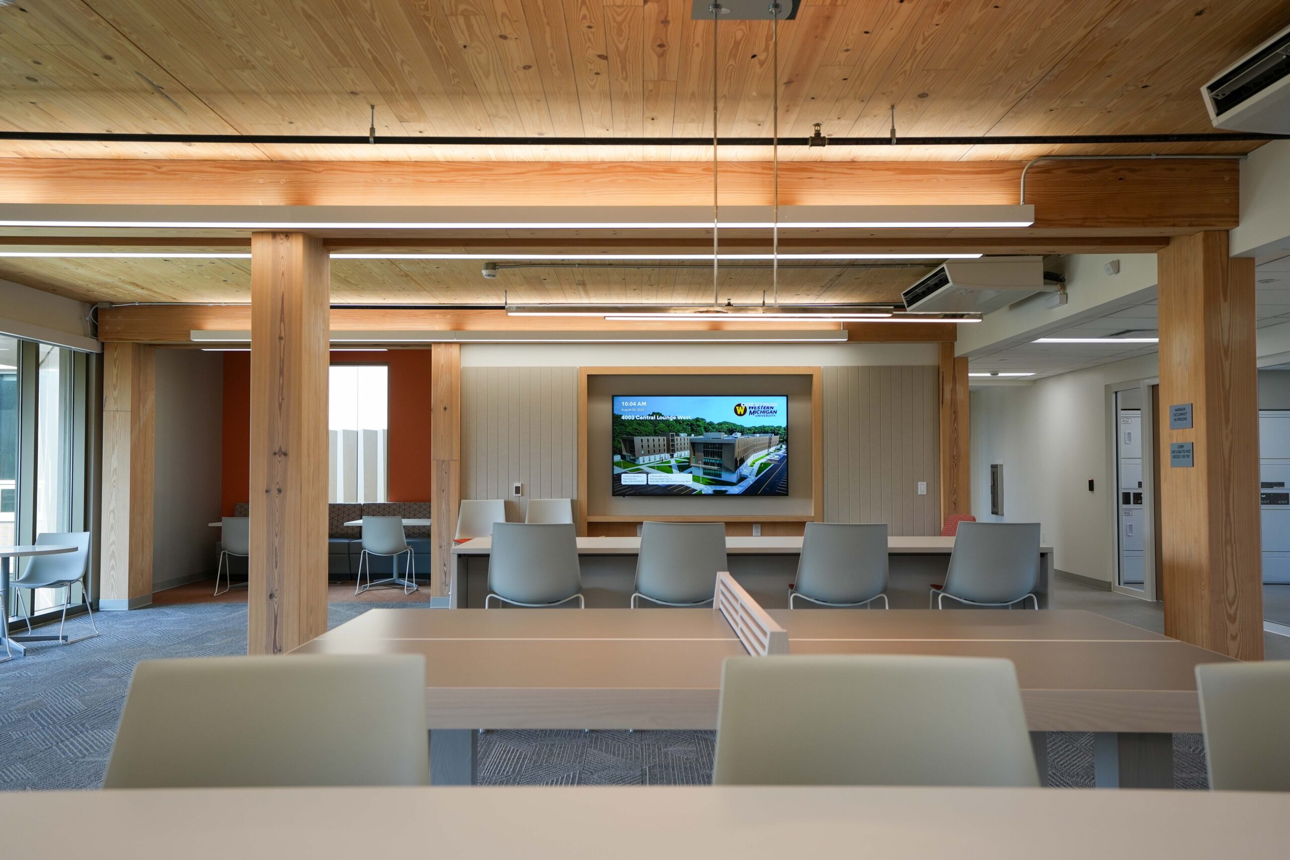 Western Michigan University Valley Oaks commons area with lounge seating, floor-to-ceiling windows, exposed timber columns, and a digital display.