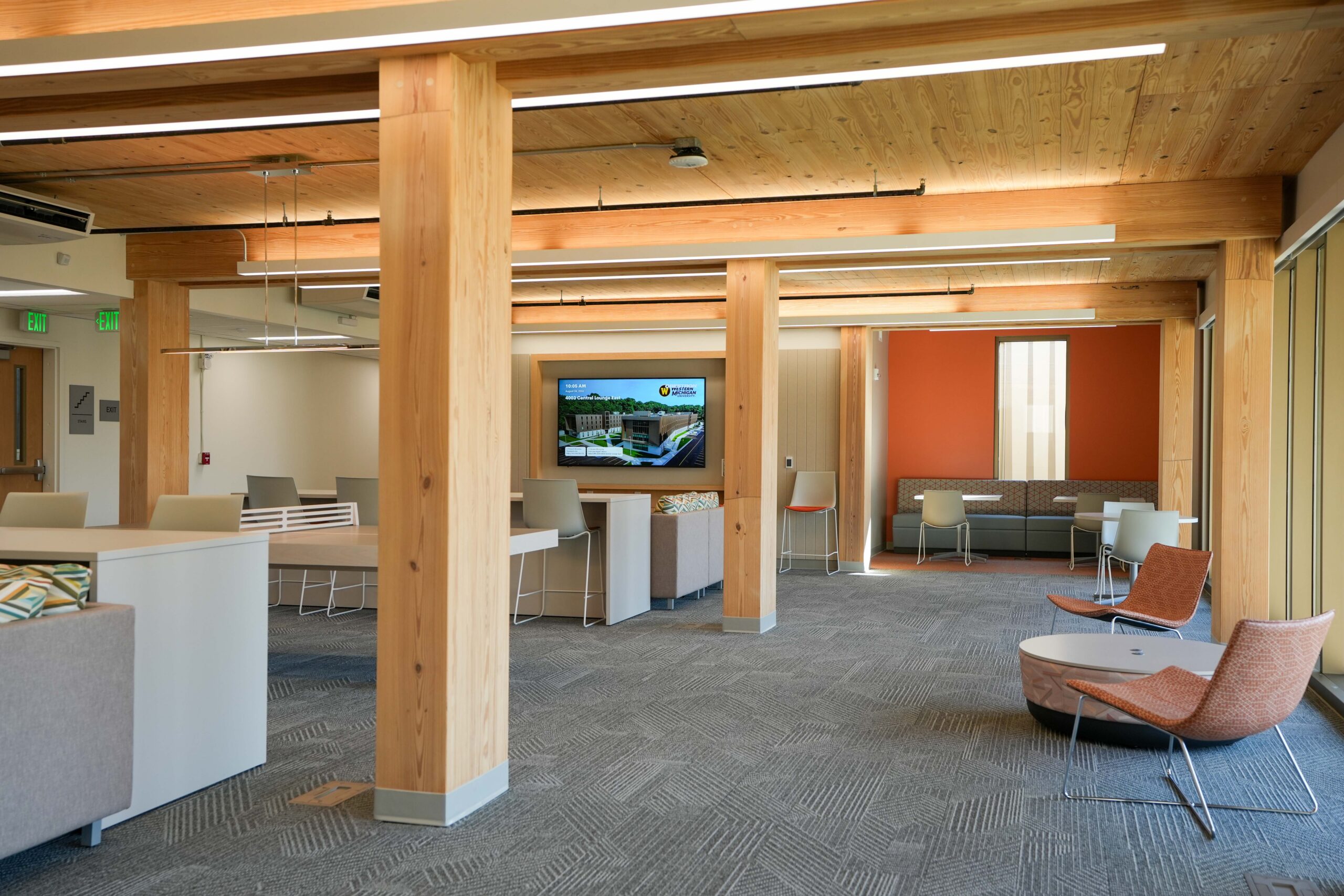 WMU Valley Oaks student lounge with exposed mass timber columns, lounge seating, and a wall-mounted digital display.